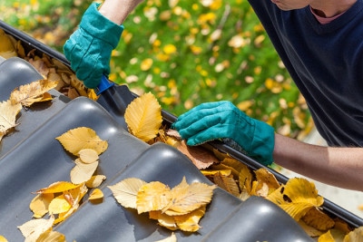 person scooping out leaves and debris from the gutter