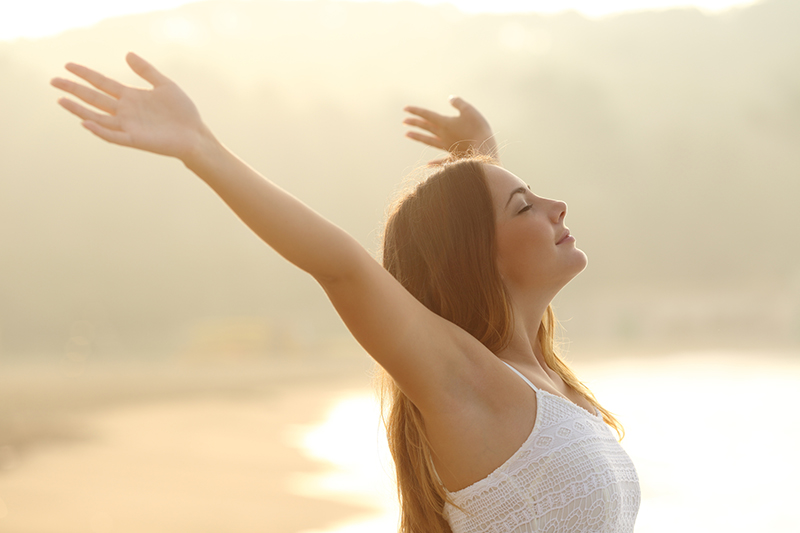 Relaxed woman breathing fresh air raising arms at sunrise with a warmth golden background